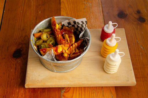 A top view of a Mexican food in a bucket with three condiment bottles on the side
