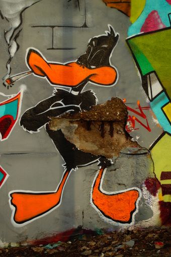 A graffito of Daffy Duck, damaged by corrosion on a bridge foundation in Frankfurt, Germany. The artist lets Daffy smoke a joint.
