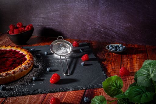 A half of wildberry cake with raspberries and blueberries on a black tray.
