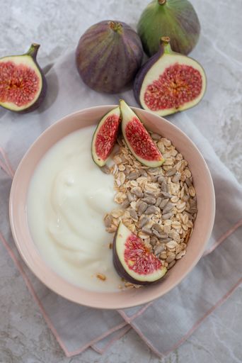 A vertical closeup shot of the granola with Greek yogurt, seeds, oats and figs on the marble table
