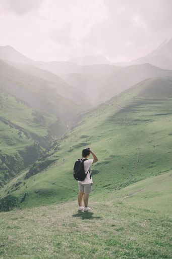 A vertical shot of a male standing in a green beautiful field on a sunny day