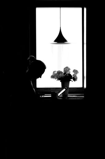 A grayscale shot of woman's silhouette working on laptop from home