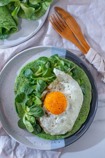 A vertical shot of delicious fried egg served with green colored pancake and spinach