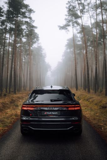 A vertical shot of a black Audi RS Q8 on the road in a foggy forest
