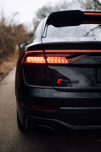 A vertical shot of a black Audi RS Q8 on the road in a foggy forest
