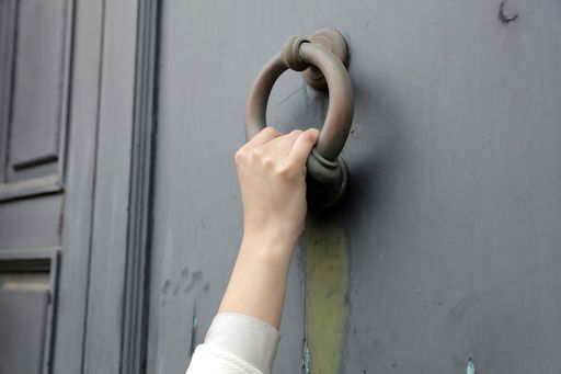 A closeup shot of a person knocking on the door with an old door knocker