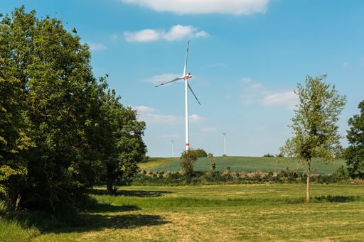 A view of a windmill in a field under the blue sky and white clouds