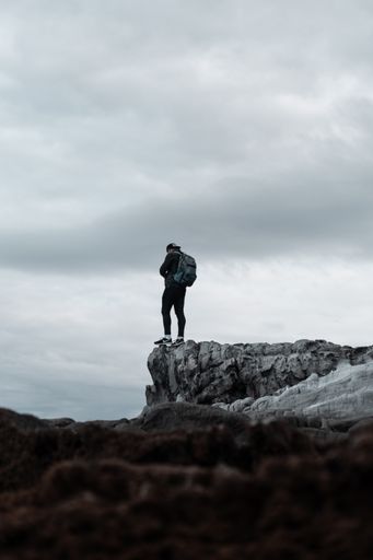 A vertical shot of a person wearing backpack standing at the edge of a gray cliff
