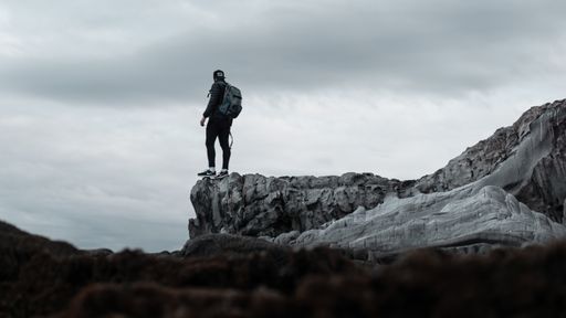 A selective shot of a person wearing backpack standing at the edge of a gray cliff