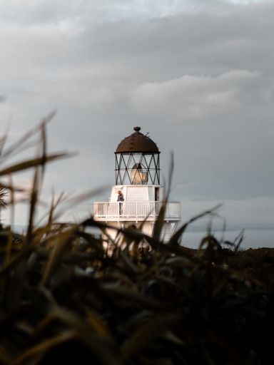 A vertical selective shot of a person standing in a brown and white lighthouse under a cloudy sky