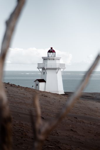 A vertical selective shot of a white lighthouse on a sandy seashore