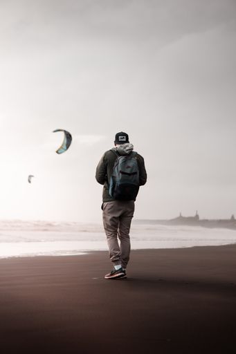 A vertical selective shot of a person wearing a cap and backpack standing on a sandy seashore