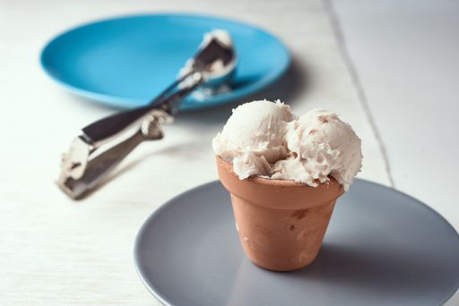 A selective focus shot of ice cream on a gray plate with an ice cream spoon on the background