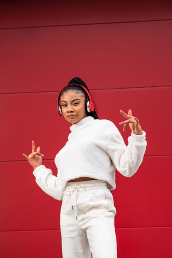 A Cheerful African American girl with long black hair dressed in sportswear listening to music with headphones on a red background