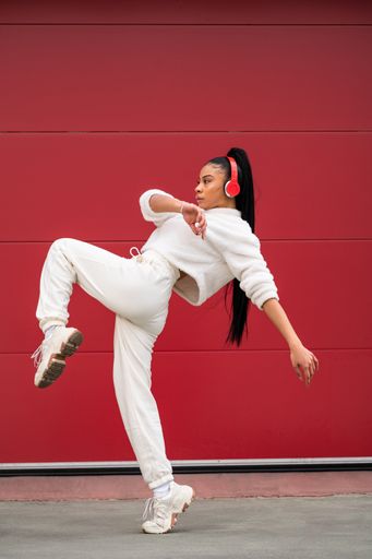 A Cheerful African American girl with long black hair dressed in sportswear listening to music with headphones on a red background