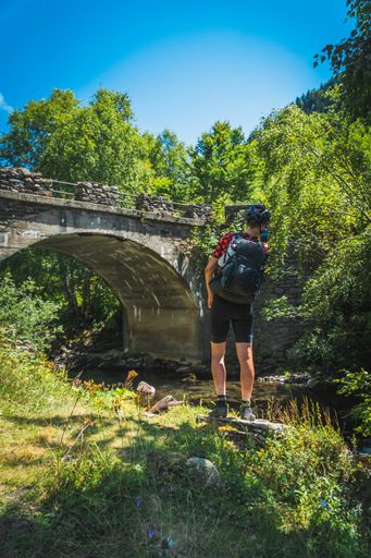 A vertical shot of the hiker taking photos of the river and the bridge in Pyrenees, Spain