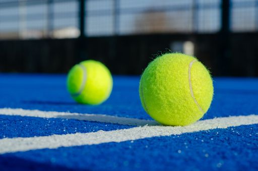 A close-up shot of a ball on the line of a tennis court with blue synthetic grass