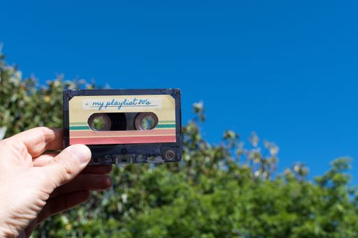 A hand holding a pair of audio cassette with the inscription my playlist 80's with blue copyspace.