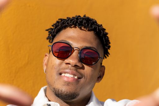 Closeup of a black Latino man wearing sunglasses posing for pictures in front of a background