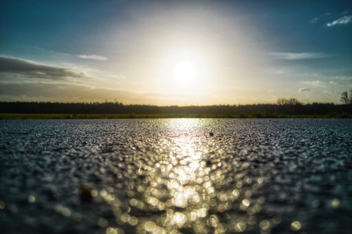 A closeup shot of an asphalt ground with the sun shining in the sky
