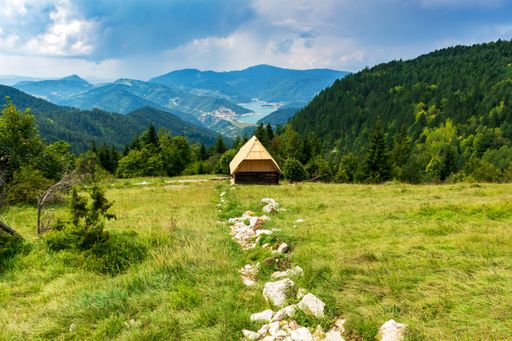 The old wooden house in the field with the lake and mountains in the background