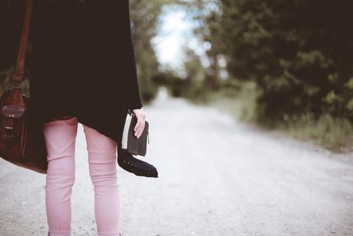 A selective closeup shot of a female wearing black jacket and a brown bag holding thick notebook standing on a road