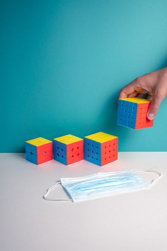 A vertical shot of a person putting different sizes of Rubik's Cube on the table near a facemask - quarantine concept