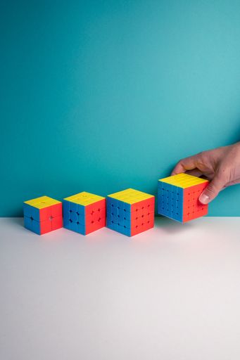A vertical shot of a person putting different sizes of Rubik's Cube on the table against a blue background