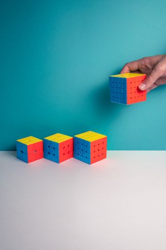 A vertical shot of a person putting different sizes of Rubik's Cube on the table against a blue background