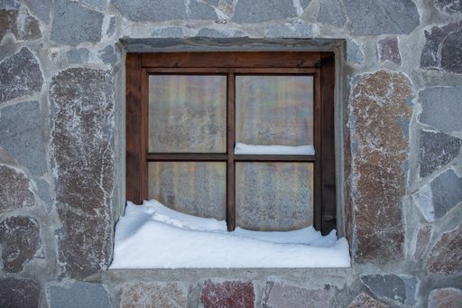 A closeup of a window of a rural house with snow on the windowsill