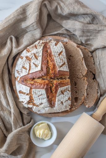 A vertical overhead shot of sliced whole grain bread, butter, and rolling pin on the table
