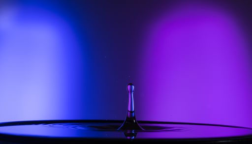 A horizontal shot of a single water drop with purple and blue lighting