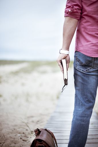 A vertical selective closeup shot of a person wearing pink shirt and jeans holding a thick notebook standing near a brown bag