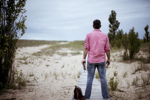 A male standing on the wooden pathway ear his bag while holding the bible with a blurred background