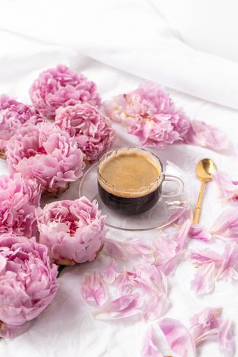 A vertical shot of a cup of instant coffee on the table with pink peonies under the lights