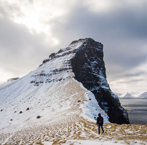 A beautiful view of a hiker male in front of a high snowy rocky hill against a light blue sky