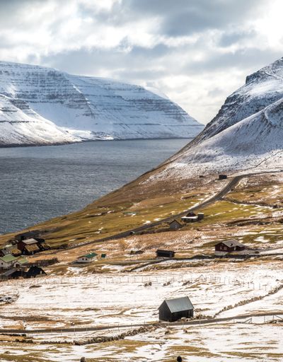 A beautiful view of ake water between snowy rocky hills against a dramatic gray sky