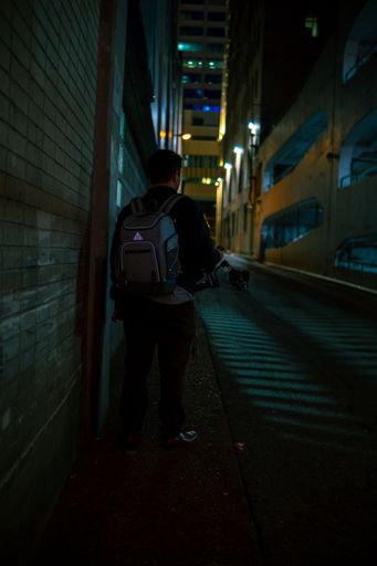 A vertical shot of a man with a backpack walking on a sidewalk in Nashville at night