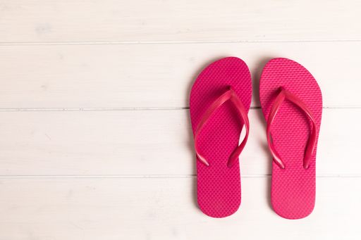 A top view of a pink flip flops on white wooden background with copy space