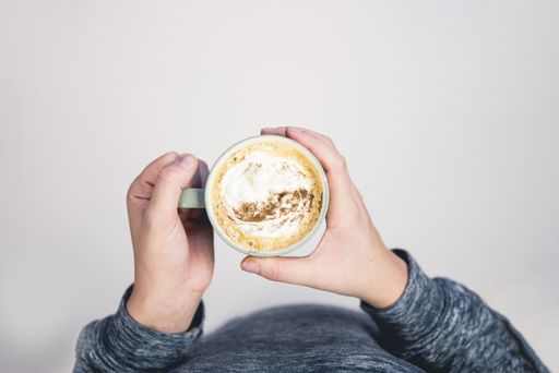 An overhead selective shot of a person holding a ceramic cup filled with latte art coffee on white background