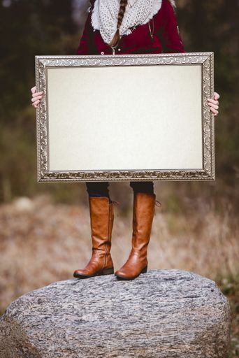 A selective vertical shot of a person holding a blank picture frame as a space for your text