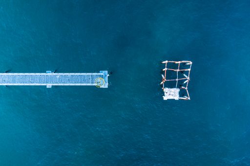 A high angle shot of a long pier over blue sea water near a lighthouse in Barcelona