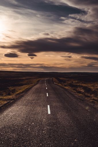 A beautiful view of an empty road with fields under the cloudy sky