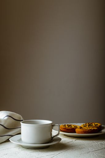 A vertical shot of cookies and a white mug on plates on a white table against a beige background with copy space