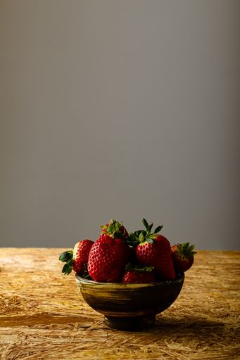 A vertical closeup of strawberries in a bowl on a rustic table against a beige background with copy space