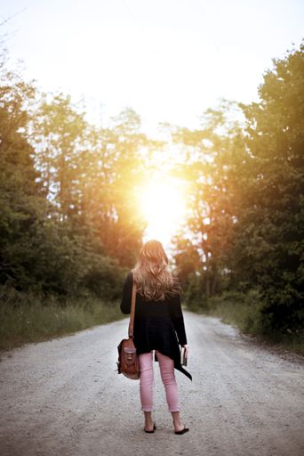 a vertical shot from behind of a female standing on an empty road while holding the bible