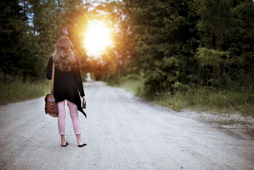 A selective shot of a female with brown bag standing in the middle of a path surrounded by trees during sunrise