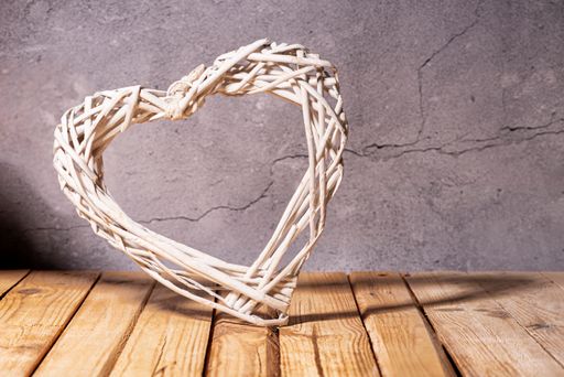 Wicker heart on wooden table, stone wall