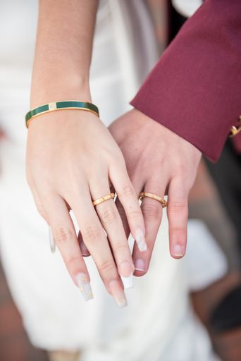 A vertical shot of a husband and wife wearing matching Versace wedding bands and rings