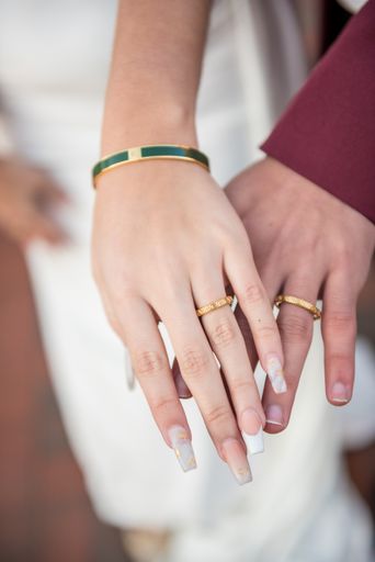 A vertical close-up shot of bride and groom hands wearing Versace rings